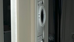 Ein Waschraum mit einer Frontlader-Waschmaschine und einem Trockner, einem Fliesenboden und einer Glastür, die in einen anderen Raum führt.