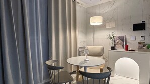 Ein moderner Essbereich mit einem runden Tisch und zwei Stühlen, einer Pendelleuchte, einer Couch und einem an der Wand befestigten Fernseher.