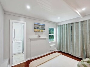 A bedroom with a bed, a window with curtains, a mounted television, and a door leading to a bathroom.