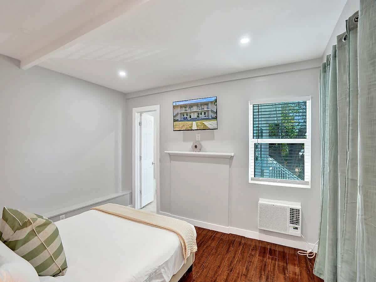 Un dormitorio con cama, ventana con persianas, aire acondicionado de pared y una puerta.