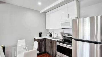 A modern kitchen with white cabinets, stainless steel appliances, and a wooden floor.