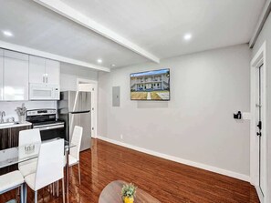 Una cocina moderna con gabinetes blancos, electrodomésticos de acero inoxidable y un comedor con sillas blancas.