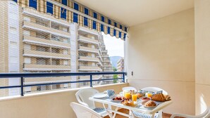 Un balcón con una mesa dispuesta para el desayuno, con cruasanes, fruta y zumo de naranja.