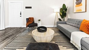 A living room with a grey sofa, a round wooden coffee table, a black armchair, a striped rug, and a large plant. - Walk to Globe Life Field & AT&T Stadium - Free Parking - 2BR Sleeps 6 (Arlington)