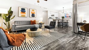 A modern living room with a grey sofa, a coffee table, and a dining area with a bar. - Walk to Globe Life Field & AT&T Stadium - Free Parking - 2BR Sleeps 6 (Arlington)