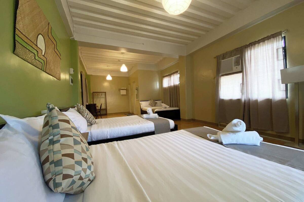 Une chambre d’hôtel avec trois lits, une salle de bain et une grande fenêtre avec des rideaux.