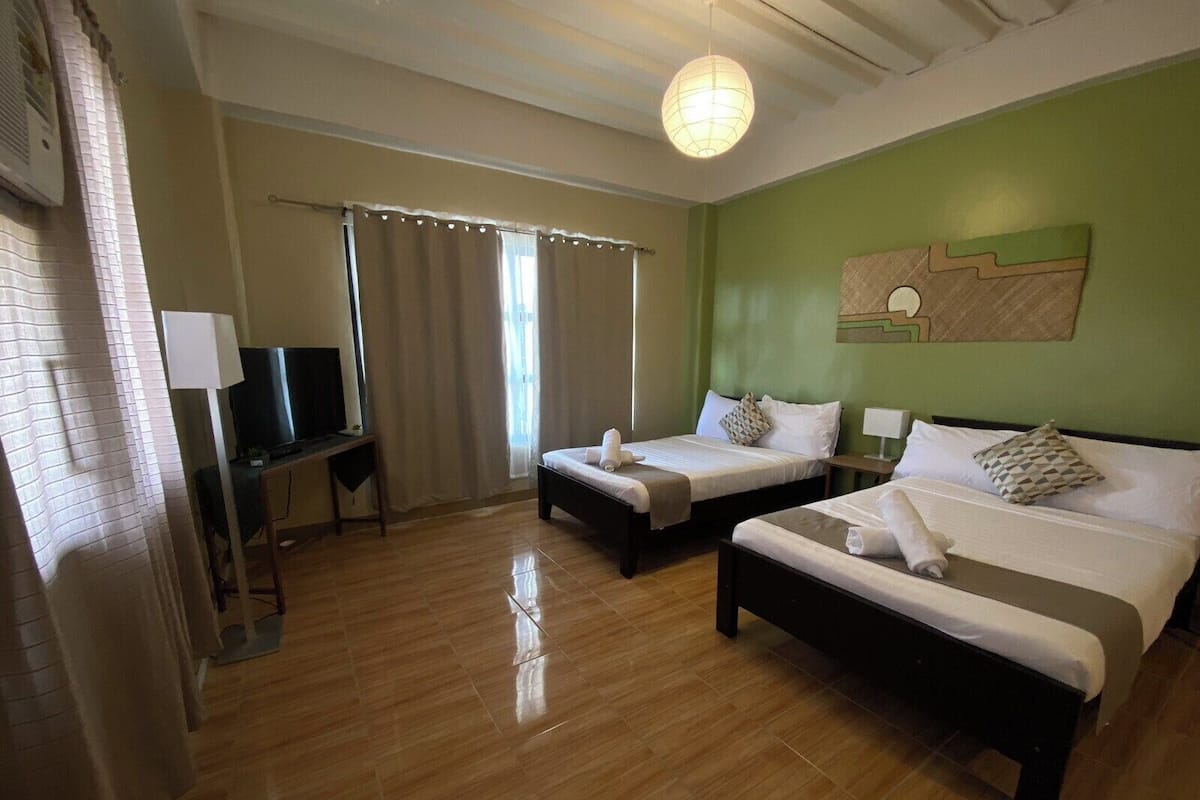 Une chambre d’hôtel avec deux lits, une télévision, un bureau et un mur vert.