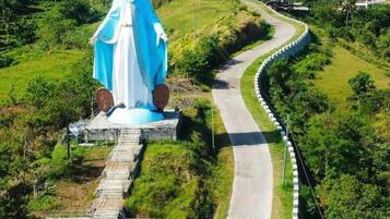 A statue of a religious figure on a curved road surrounded by lush greenery.
