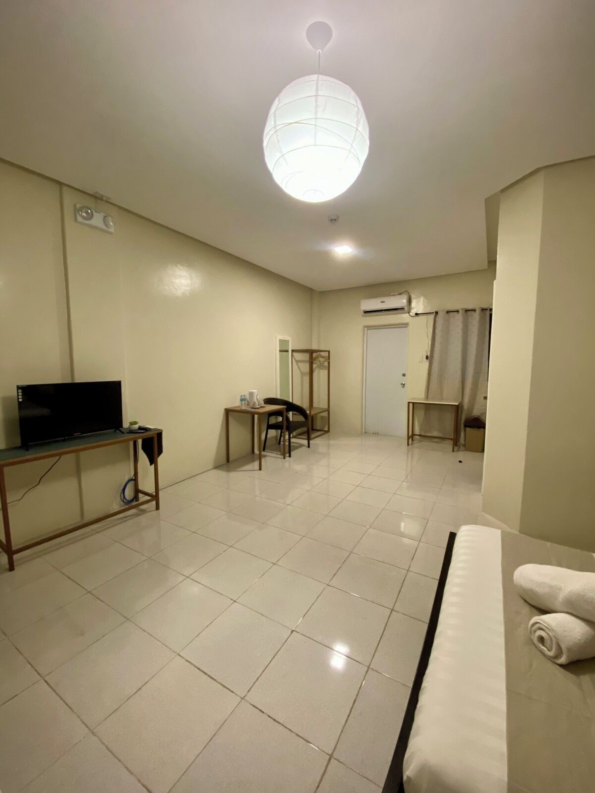 Une chambre d’hôtel comprenant un lit, un bureau avec une télévision, une chaise, une petite table avec une tasse et un luminaire suspendu.