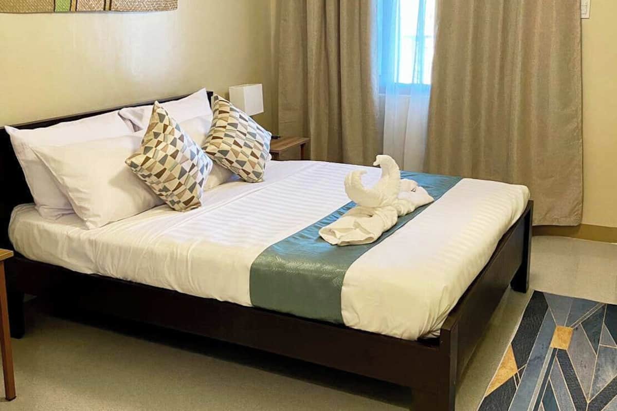 Un lit bien fait, avec du linge de lit blanc, des coussins à motifs et une serviette décorative en forme de cygne.
