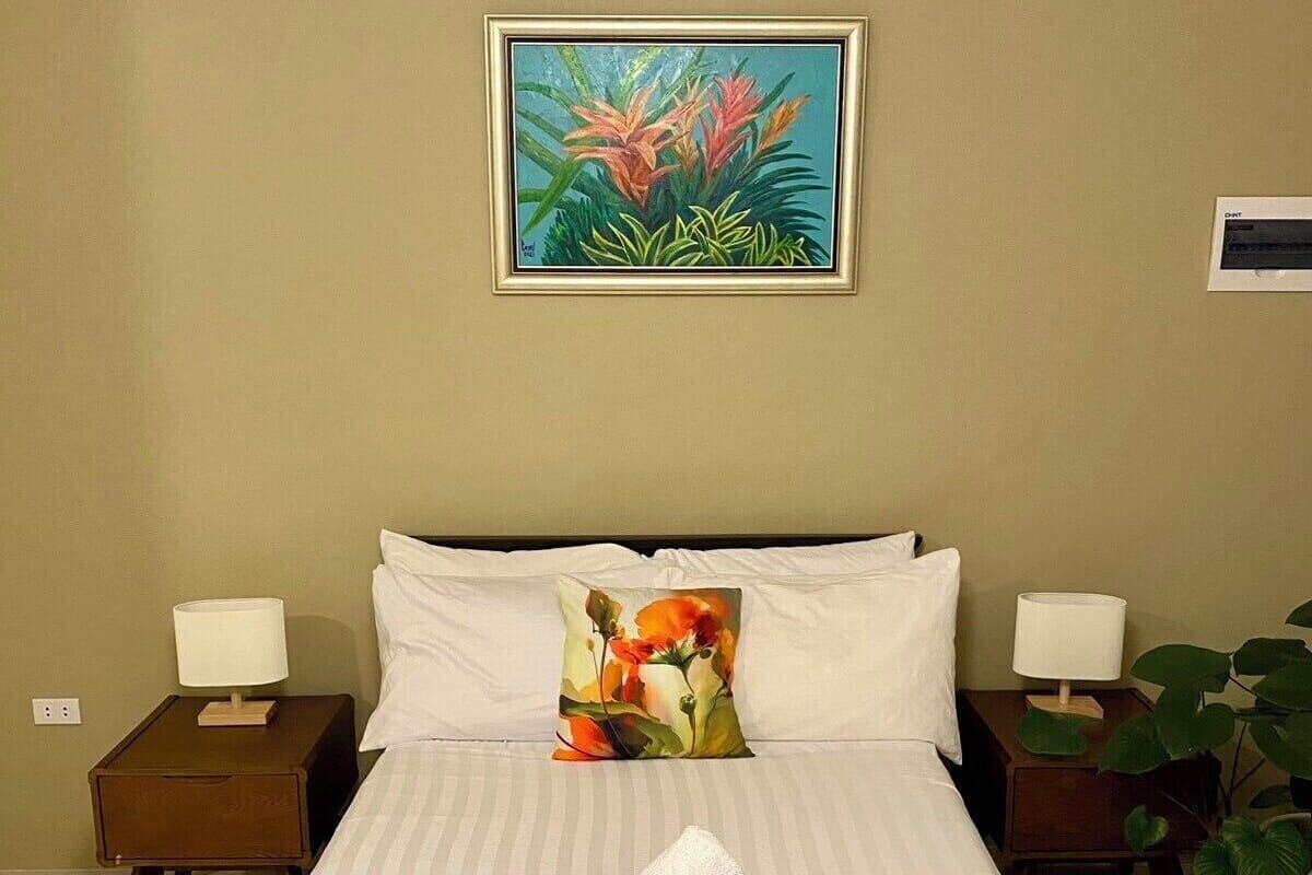 Une chambre d’hôtel avec un lit, deux tables de chevet, un tableau et une plante en pot.
