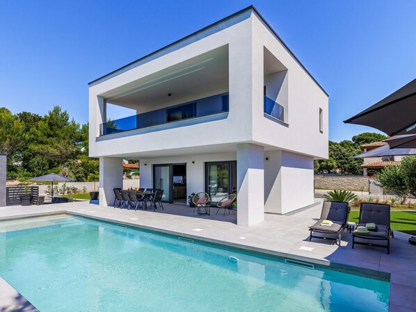 Une maison moderne à deux étages, dotée d’une piscine, d’un espace extérieur aménagé et offrant une vue sur le paysage environnant.