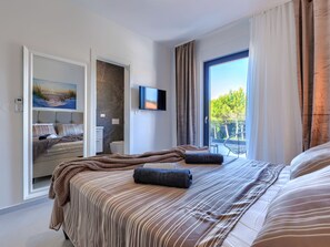 Une chambre d’hôtel moderne dotée d’un grand lit, d’une télévision et d’un balcon offrant une vue sur les arbres.