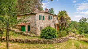 A stone house with green shutters, a tiled roof, and a stone wall surrounding the property.