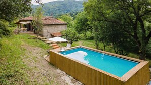 A wooden swimming pool with a view of a stone building and trees.
