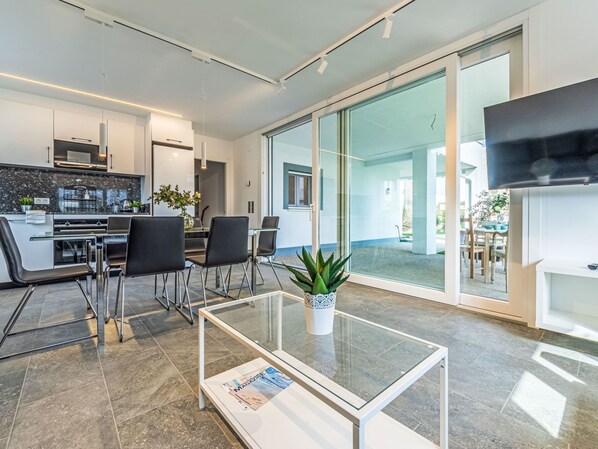 A modern kitchen with a dining area, a glass coffee table, and a TV mounted on the wall.