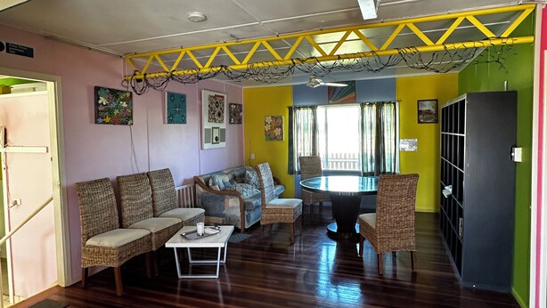 A spacious living area with a wooden floor, a sofa set, a dining table with chairs, and a yellow ceiling structure. - Star Guesthouse (Proserpine)