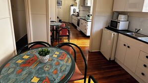 A compact kitchen with white cabinets, a microwave, and a sink. A dining area with a round table and chairs is visible in the foreground. - Star Guesthouse (Proserpine)