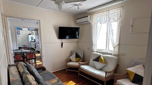 A living room with a sofa, two armchairs, a ceiling fan, a TV, and a window with curtains. - Star Guesthouse (Proserpine)