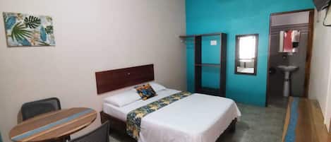Una stanza con un letto, una scrivania, una sedia, un tavolino, una ventola e un lavandino.