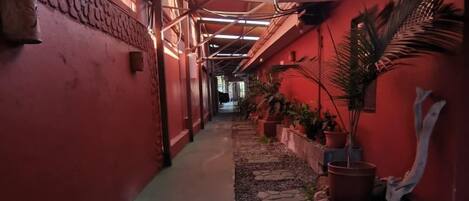 A narrow corridor with red walls, potted plants, and a tiled floor.