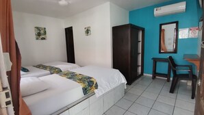 A hotel room with two beds, a wardrobe, a desk with a chair, and an air conditioning unit. - Hotel Cabinas Jacomar (Jacó)