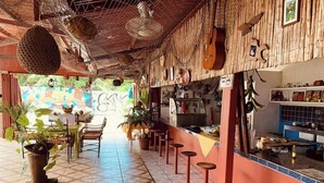 An interior with a tiled floor, a bar area, stools, and hanging decorations. - Hotel Cabinas Jacomar (Jacó)