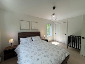 A bedroom with a bed, bedside tables, a window, a door, and a crib.