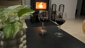 Una sala de estar acogedora con chimenea, dos copas de vino sobre una mesa y una escalera al fondo.