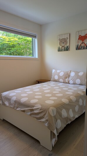 Een slaapkamer met een bed, een nachtkastje, een raam met uitzicht op bomen en twee decoratieve wandpanelen.