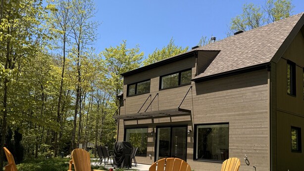 Una casa moderna de dos pisos con un patio que tiene sillas Adirondack y un brasero.