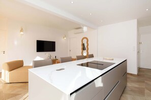 Cozinha moderna com ilha central, área de jantar com cadeiras, televisão de tela plana e espelho fixado na parede.