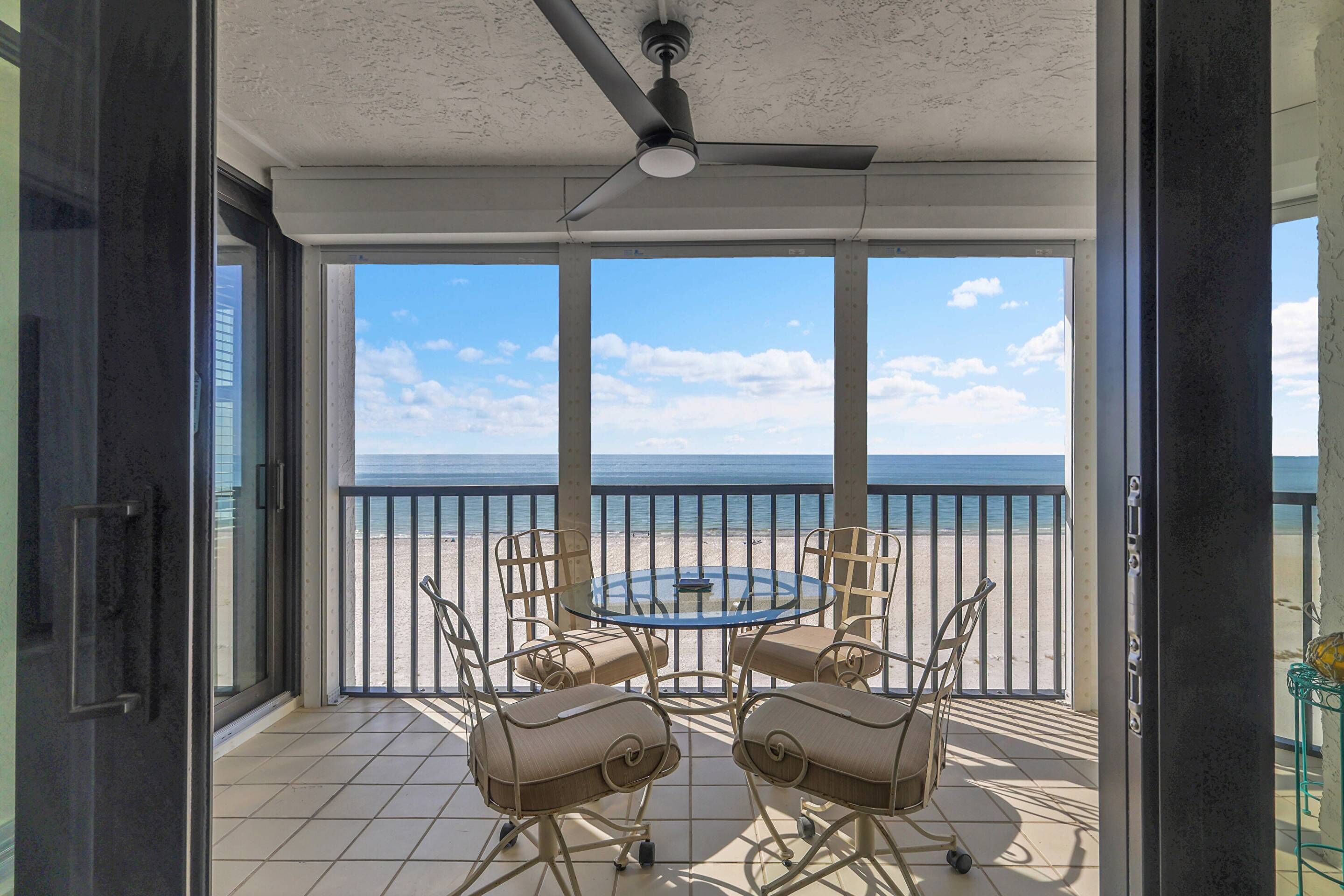 A balcony with a table and chairs, overlooking a beach and the ocean.