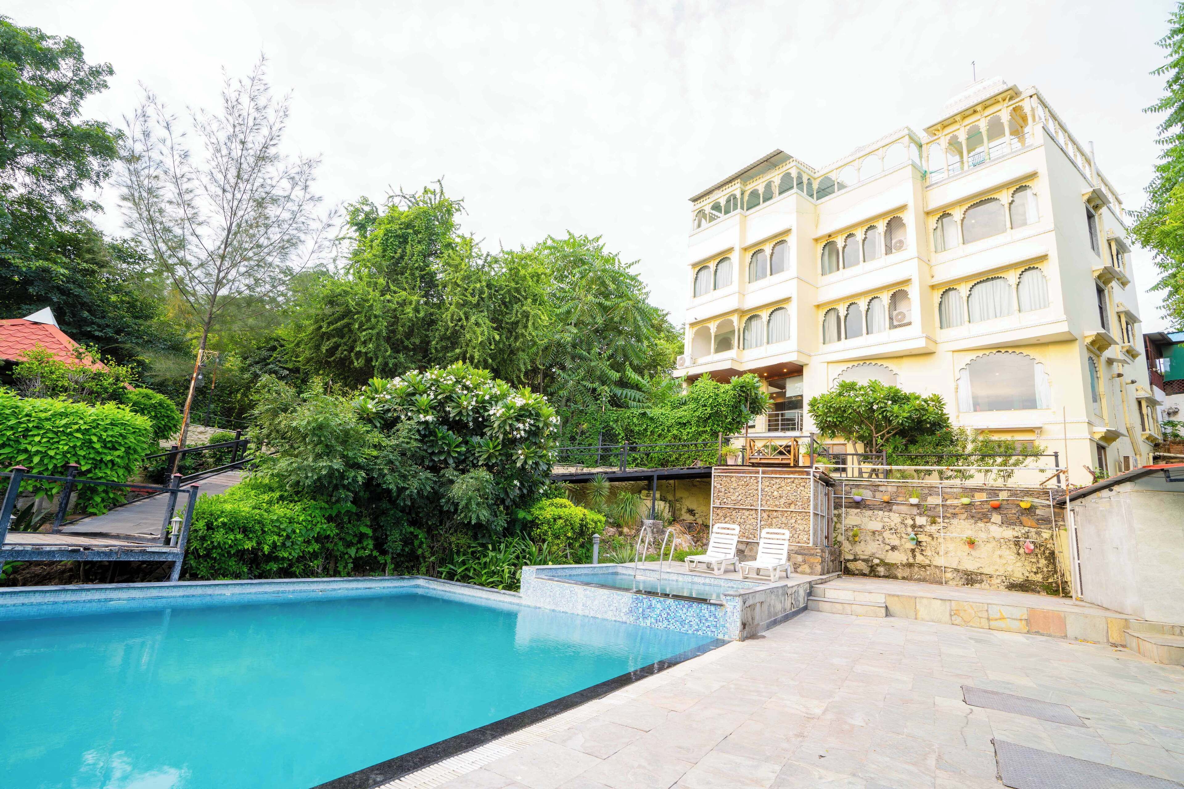 Piscina com espreguiçadeiras, rodeada por vegetação exuberante e um edifício com varandas.
