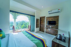 A hotel room with a bed, a TV, a desk, and a view of the outdoors. - Treebo The Aravali Getaway (Udaipur)