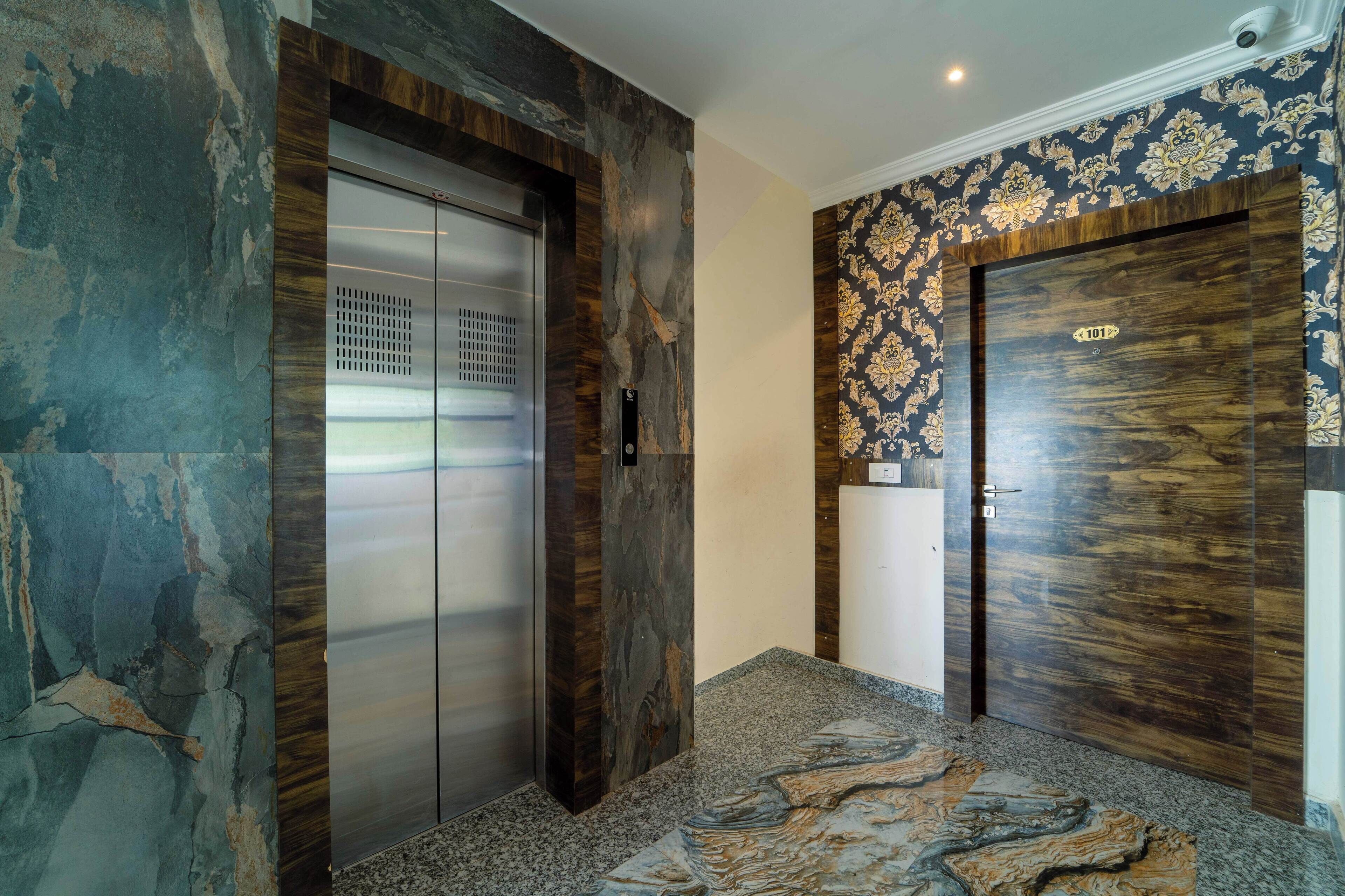 An elevator with a metallic finish, a wooden door with a number plate, and a patterned wall.