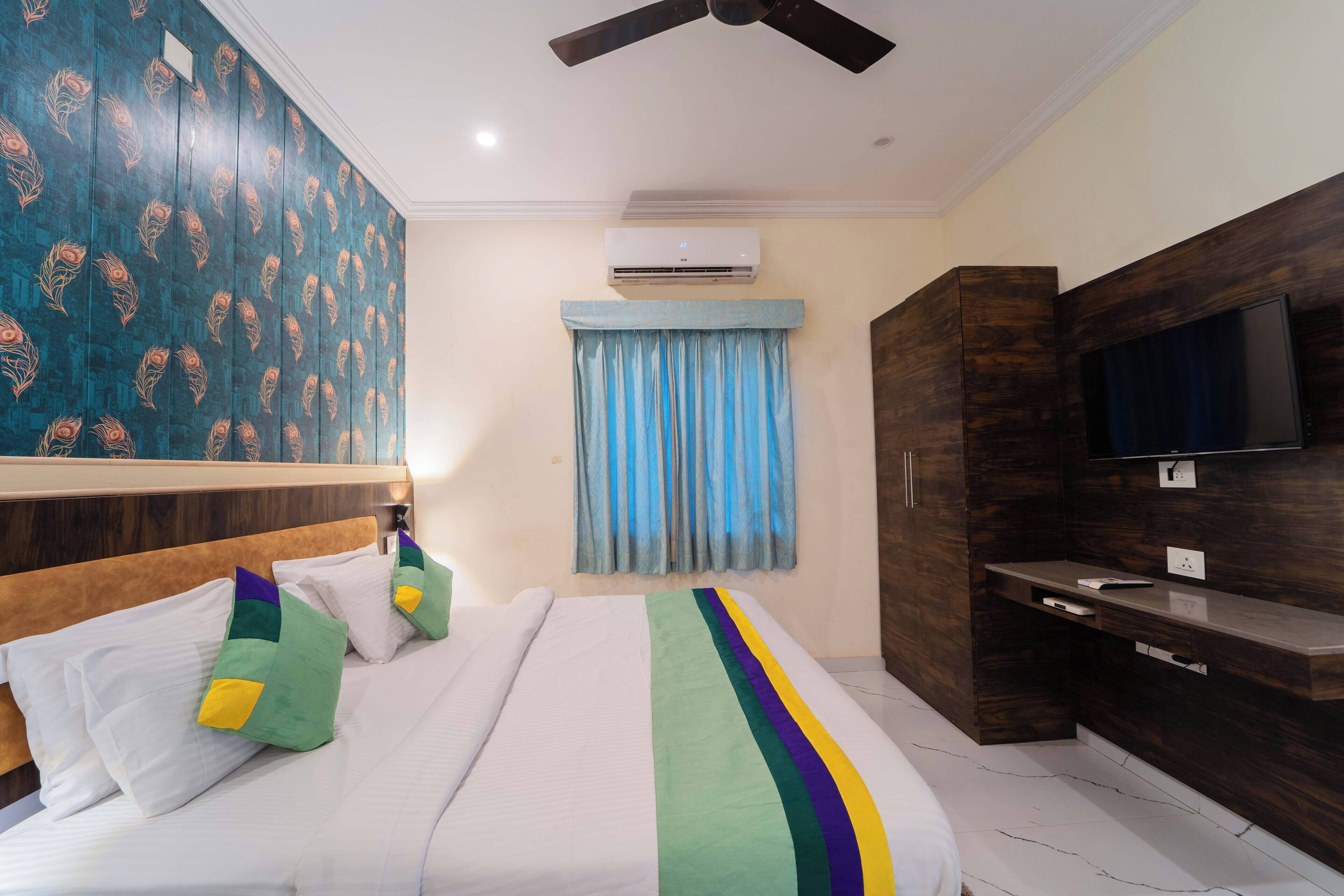 A hotel room with a bed, a TV, a wardrobe, and an air conditioning unit.