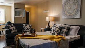 Ein Hotelzimmer mit einem Bett, einem Sofa, einem Tablett mit Gläsern, einer Lampe und einem Wandbild.