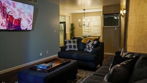 Ein Wohnzimmer mit einem dunkelblauen Sofa, einem Couchtisch mit einem Gesellschaftsspiel und einem Flachbildfernseher an der Wand.