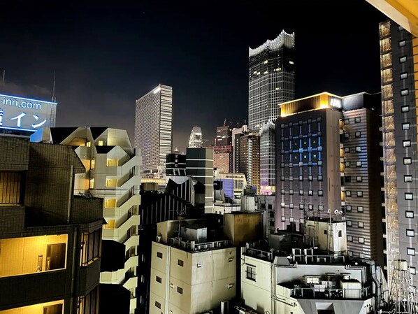 Paisaje urbano nocturno con edificios modernos, incluyendo un rascacielos destacado con un diseño único en la parte superior.