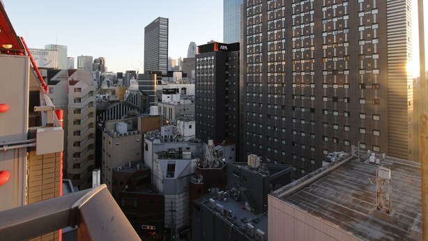 Une vue urbaine mettant en évidence un bâtiment imposant portant l’inscription « APA HOTEL », caractérisé par une façade en forme de grille avec de nombreuses fenêtres.