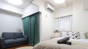 Une chambre d’hôtel moderne avec un lit, un canapé, un tapis rond et une fenêtre avec des rideaux.
