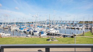 Un port de plaisance où sont amarrés de nombreux bateaux, une zone herbeuse au premier plan et un pont en arrière-plan.