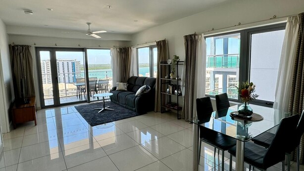 A spacious living area with a balcony, a dining table with chairs, a sofa, and a ceiling fan. - Katara on Woods (Darwin)