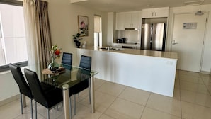 A modern kitchen with white cabinets, a stainless steel refrigerator, and a glass dining table with chairs. - Katara on Woods (Darwin)