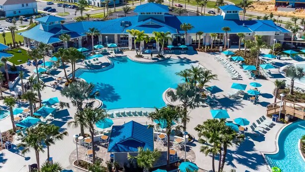 A resort with a large central pool, multiple lounge areas with umbrellas, and palm trees.
