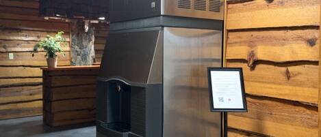 A stainless steel refrigerator with a water dispenser, placed against a wooden wall with a sign next to it.