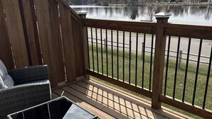 Une terrasse en bois, dotée de meubles d’extérieur, d’une rambarde et offrant une vue sur un lac.
