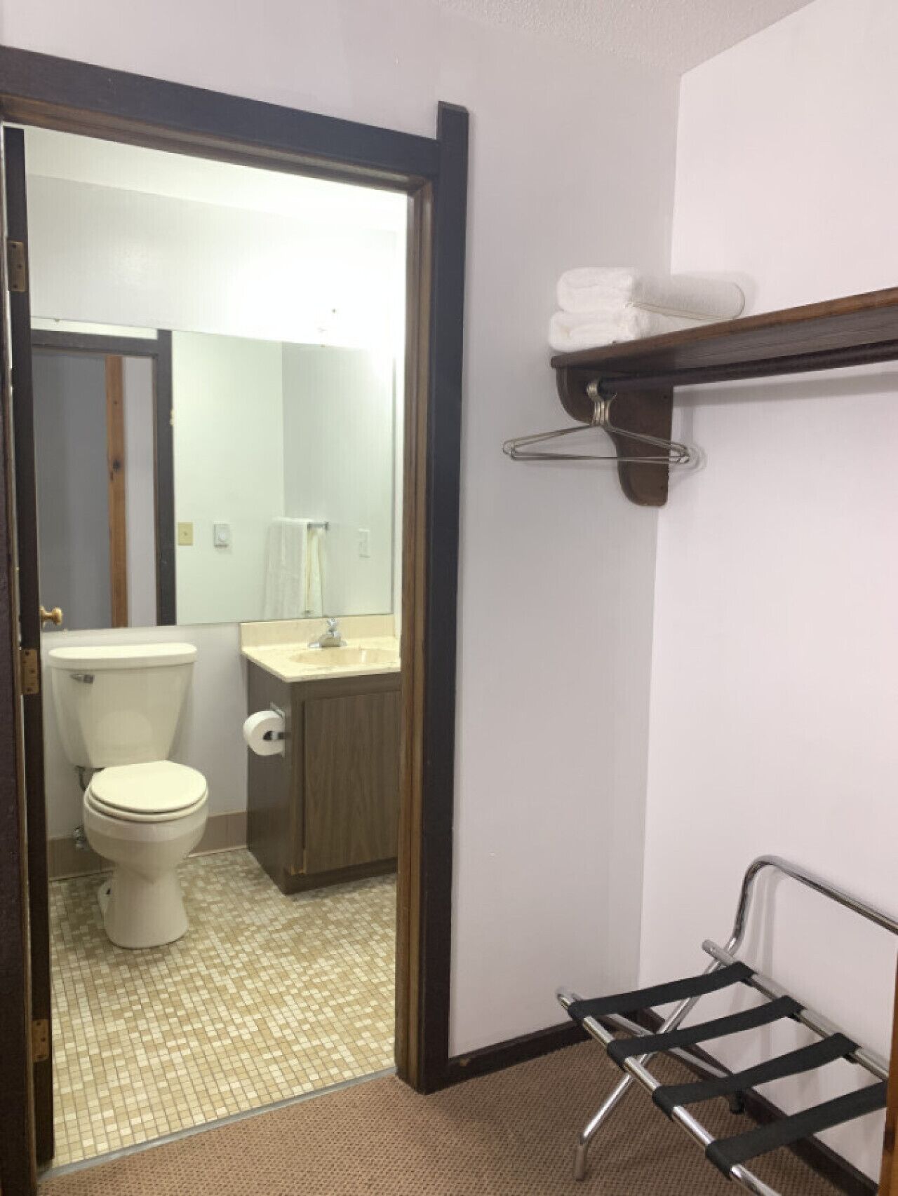 Un baño con inodoro, lavamanos y espejo. Hay un perchero sobre el lavamanos y una toalla colgada en él.