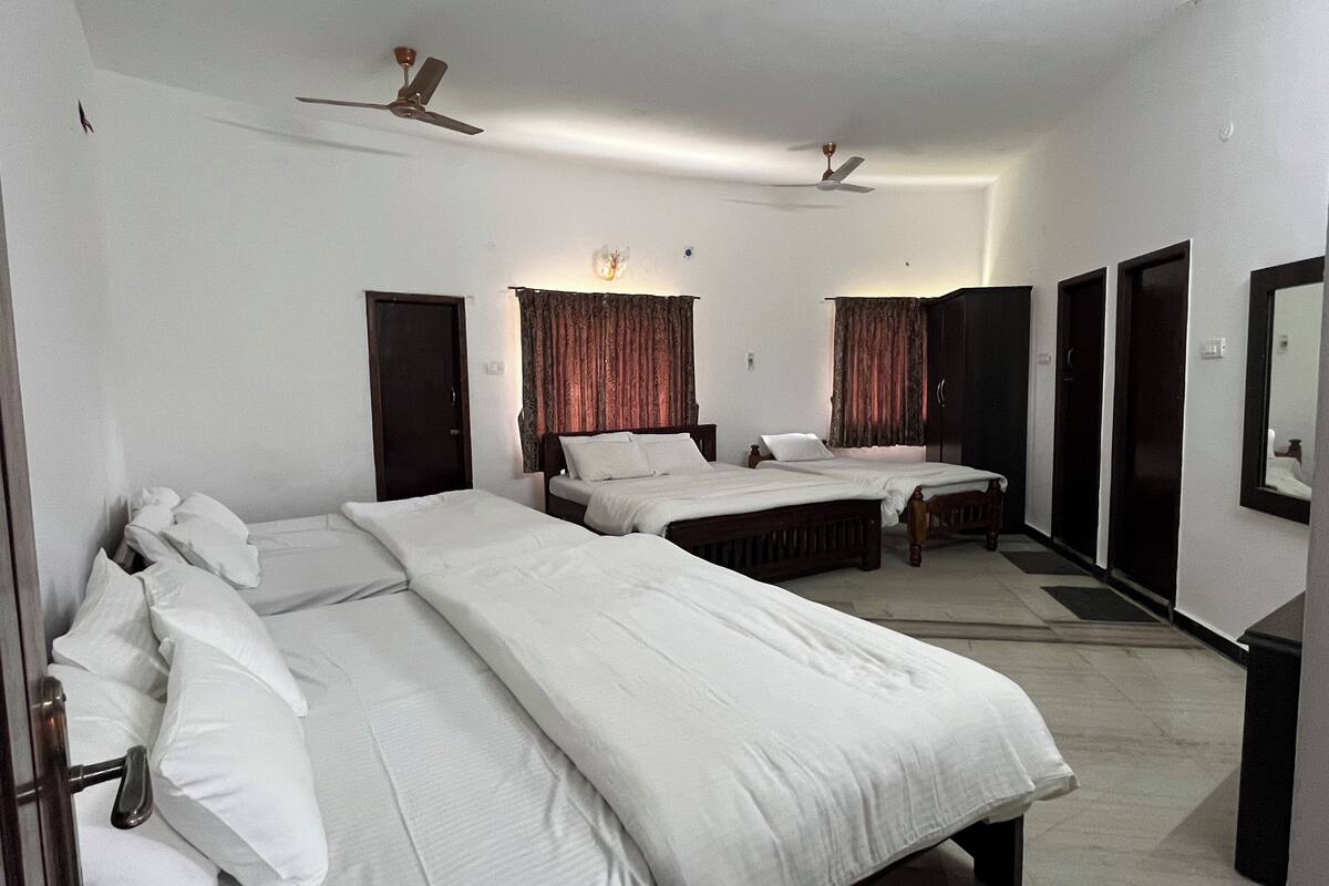 A hotel room with three single beds, a ceiling fan, a wardrobe, and a mirror.